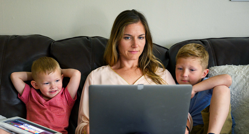 女人和她的两个孩子坐在沙发上，同时使用她的电脑。